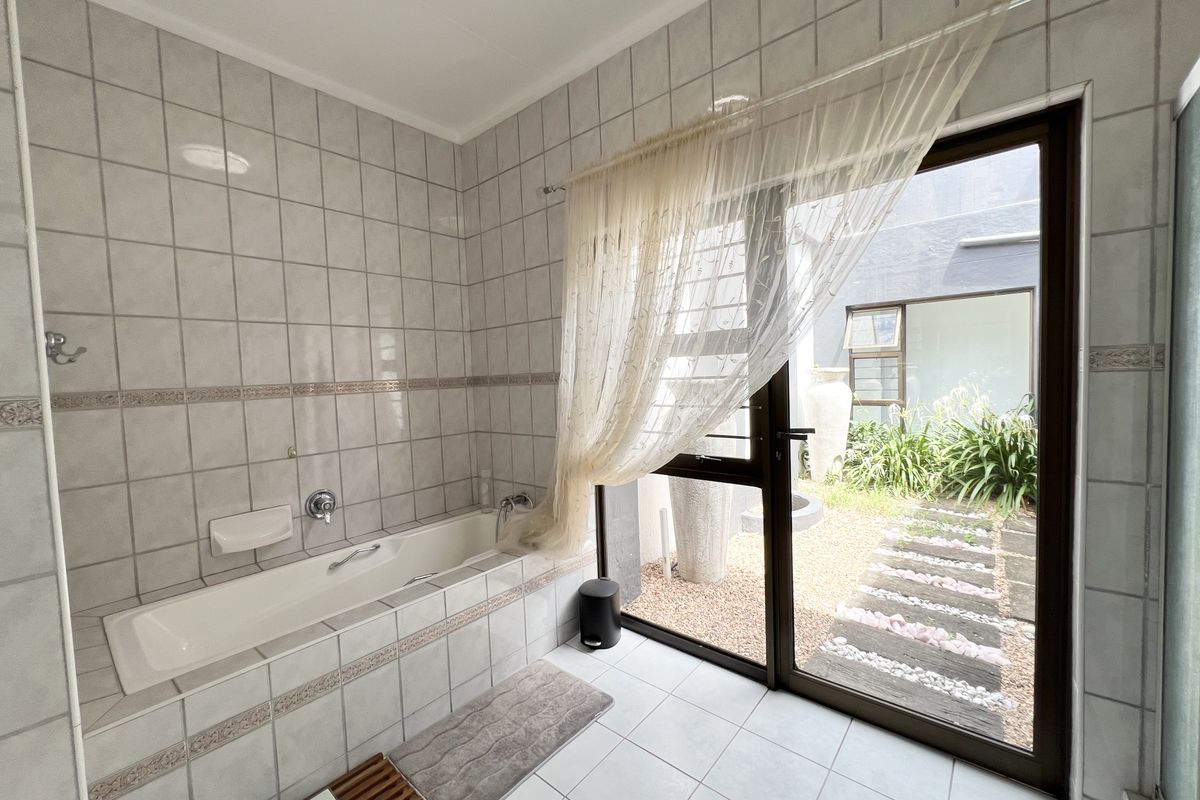 A bathroom featuring a built-in bathtub with tiled surround and direct access to a private courtyard through a sliding glass door.