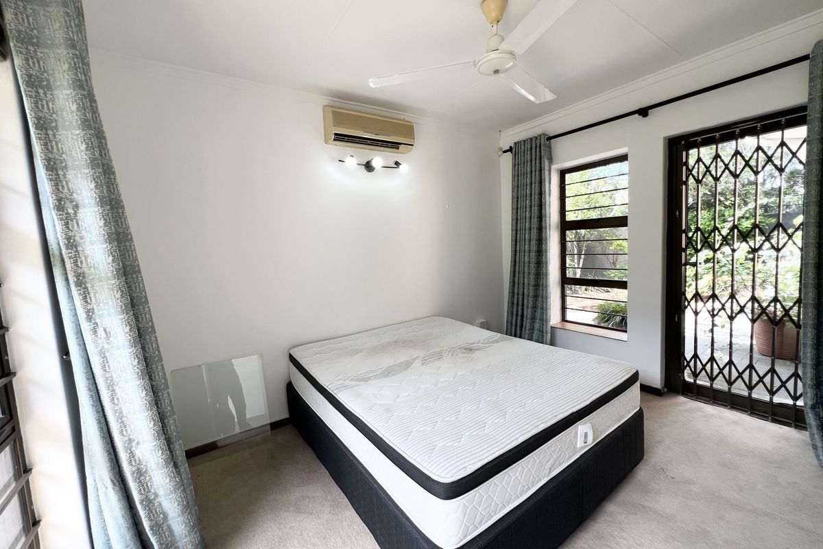 A bedroom featuring a ceiling fan, wall-mounted air conditioner, and direct access to the garden through a secure metal gate.
