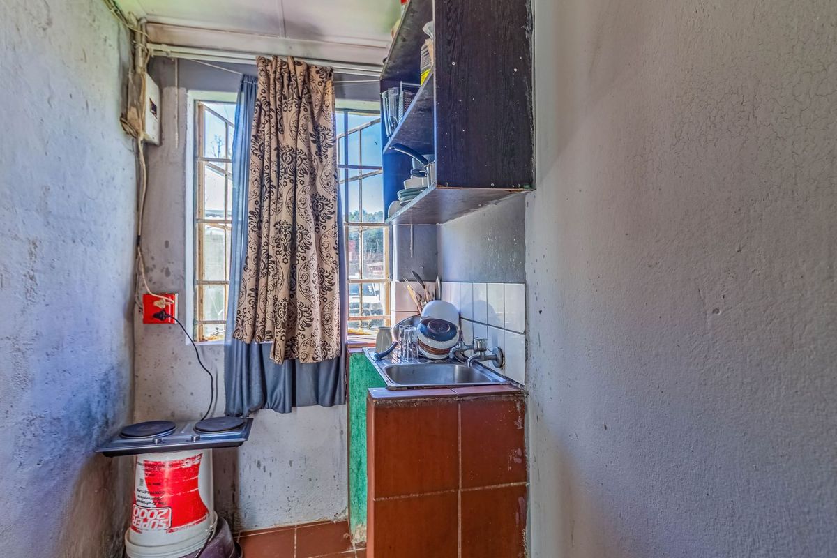 A small, basic kitchen area featuring a single sink, tiled splashback, and wall-mounted shelving, requiring significant renovation and cosmetic updates.