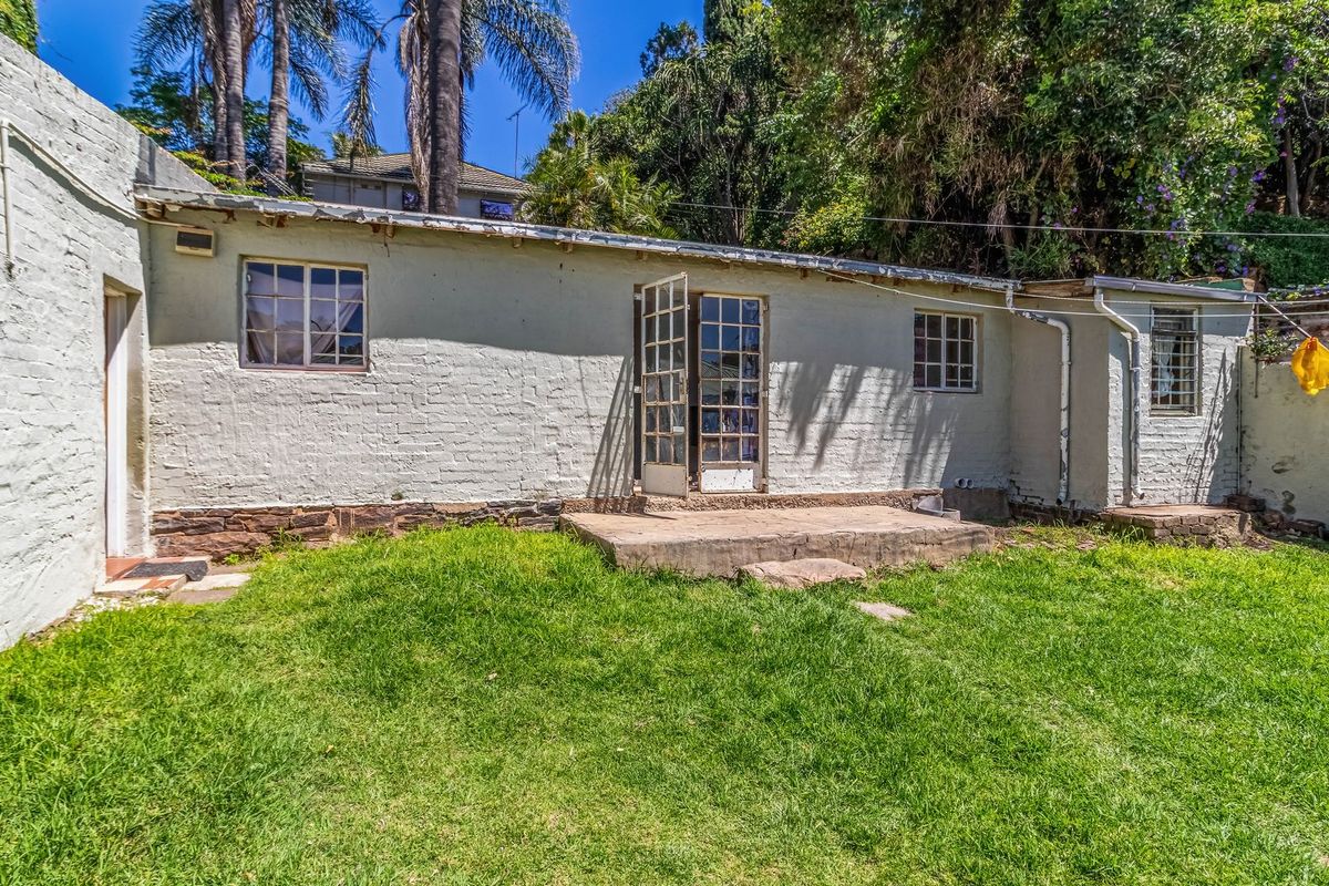 Rear exterior view of the property featuring a painted brick facade, small concrete patio area, and access to the garden.