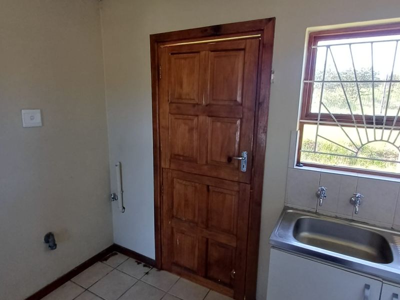 A functional laundry area featuring tiled flooring, a stainless steel sink, and a solid timber door with security gate.