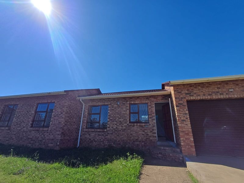 Front elevation of a face brick house featuring a single garage, security-barred windows, and a concrete entrance path under a clear blue sky.