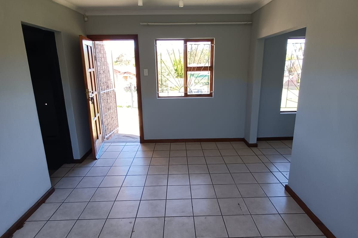 An empty, neutrally painted living area featuring tiled flooring, security bars on windows, and direct access to the exterior.