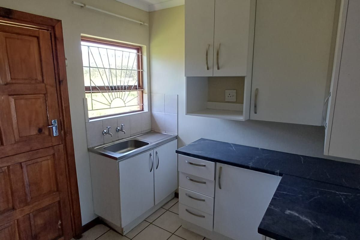 A functional kitchen featuring white cabinetry, dark laminate countertops, a stainless steel sink, and ceramic floor tiles.