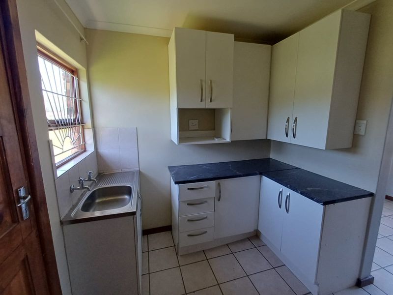 A functional scullery area featuring white built-in cabinetry, dark laminate countertops, a stainless steel sink, and tiled flooring.