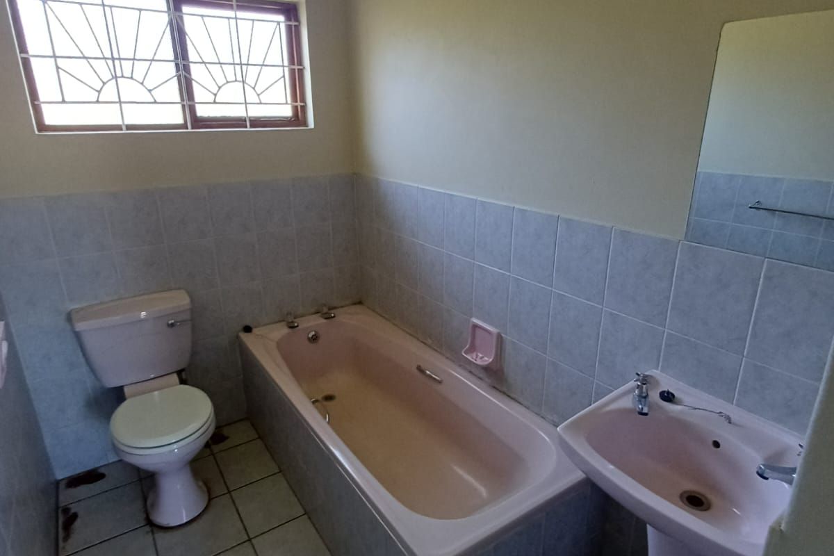 A functional bathroom featuring a bathtub, pedestal basin, and toilet with tiled finishes and security bars on the window.