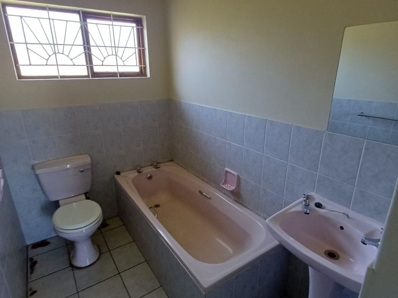 A functional bathroom featuring a bathtub, pedestal basin, and toilet with tiled finishes and security bars on the window.