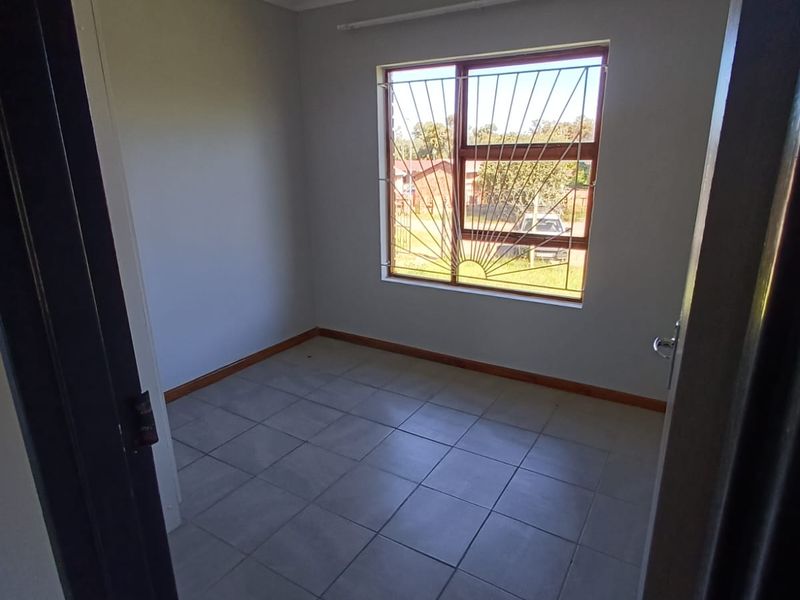 A vacant bedroom featuring neutral tiled flooring, clean walls, and a window fitted with security bars, offering a blank canvas for personalization.