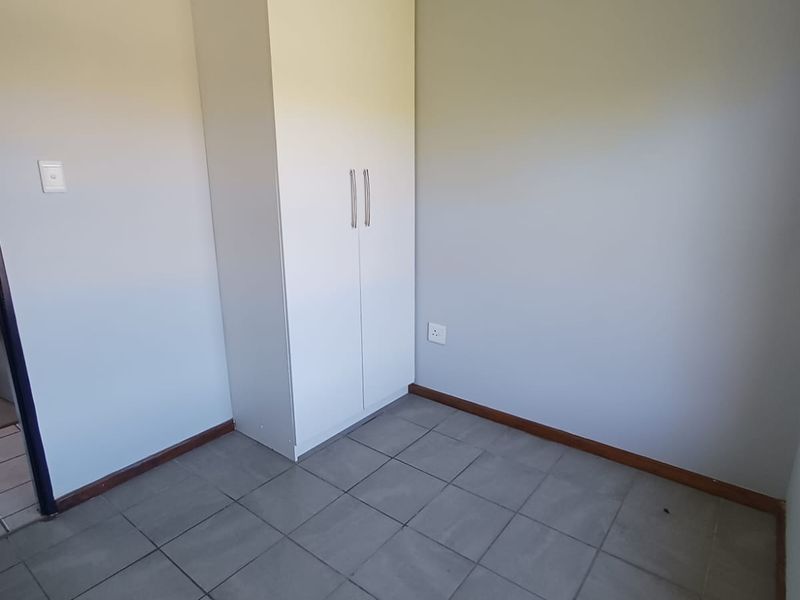 A clean, empty bedroom featuring neutral grey walls, tiled flooring, and a built-in wardrobe with modern handles.
