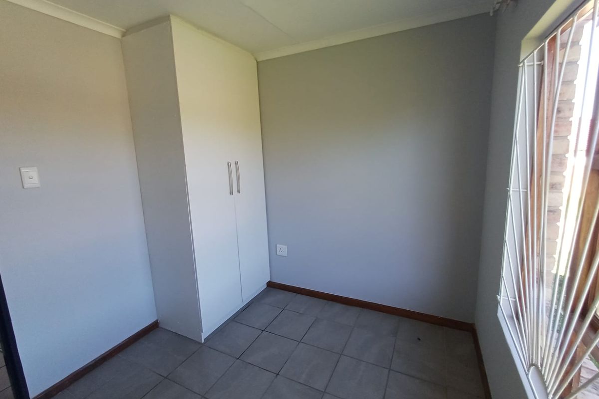 A clean, empty bedroom featuring neutral wall paint, tiled flooring, and a built-in wardrobe with modern handles.