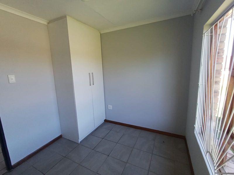 A clean, empty bedroom featuring neutral wall paint, tiled flooring, and a built-in wardrobe with modern handles.
