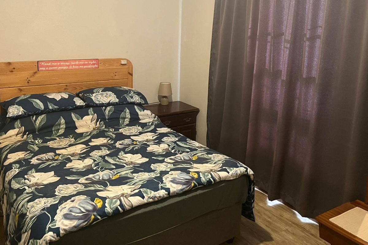 A functional bedroom featuring laminate flooring and window curtains, providing a comfortable and private sleeping space.