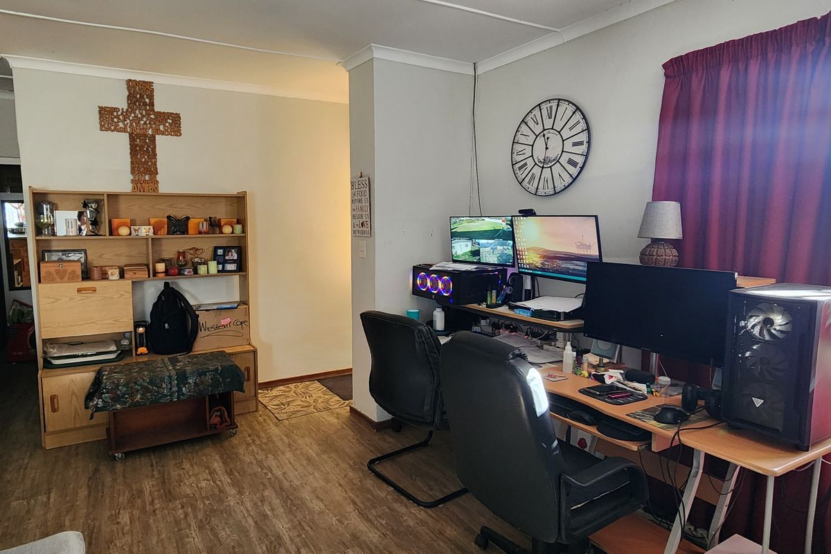A living area featuring laminate flooring and coving, currently utilized as a home office space.