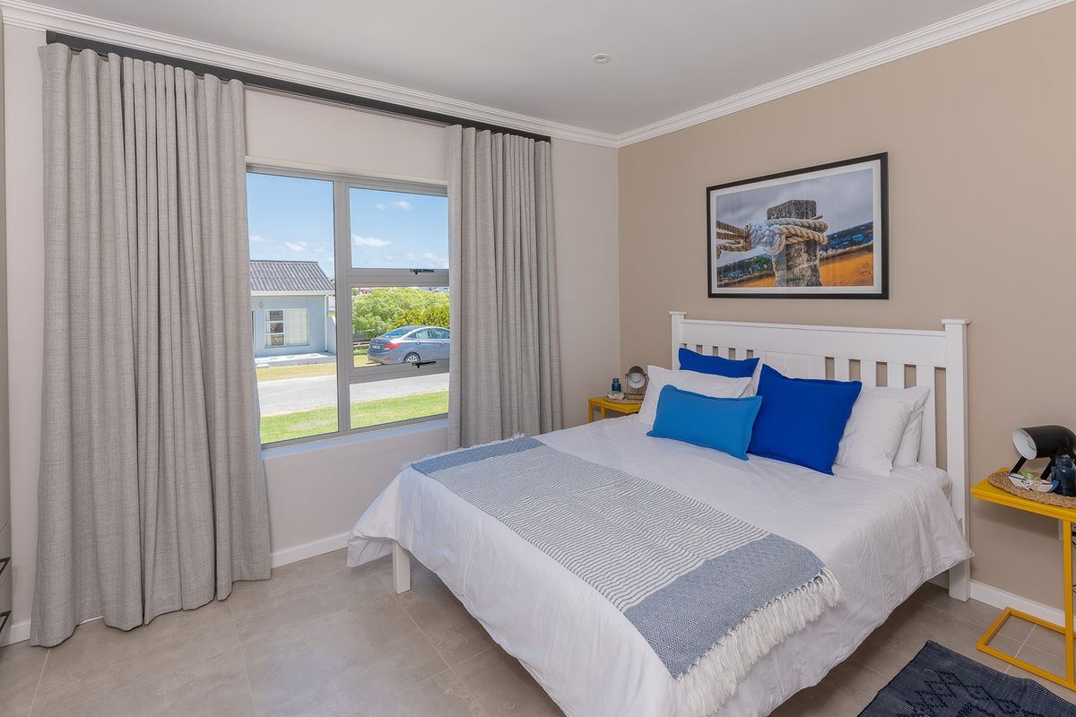 A well-maintained bedroom featuring tiled flooring, a built-in wardrobe, and large windows with neutral curtains, offering a bright and comfortable living space.
