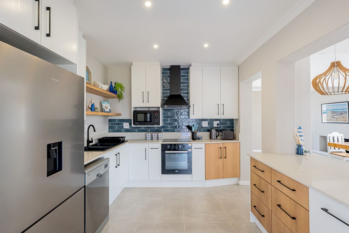 Modern kitchen featuring white and wood-tone cabinetry, quartz countertops, a blue subway tile backsplash, and high-quality built-in appliances.