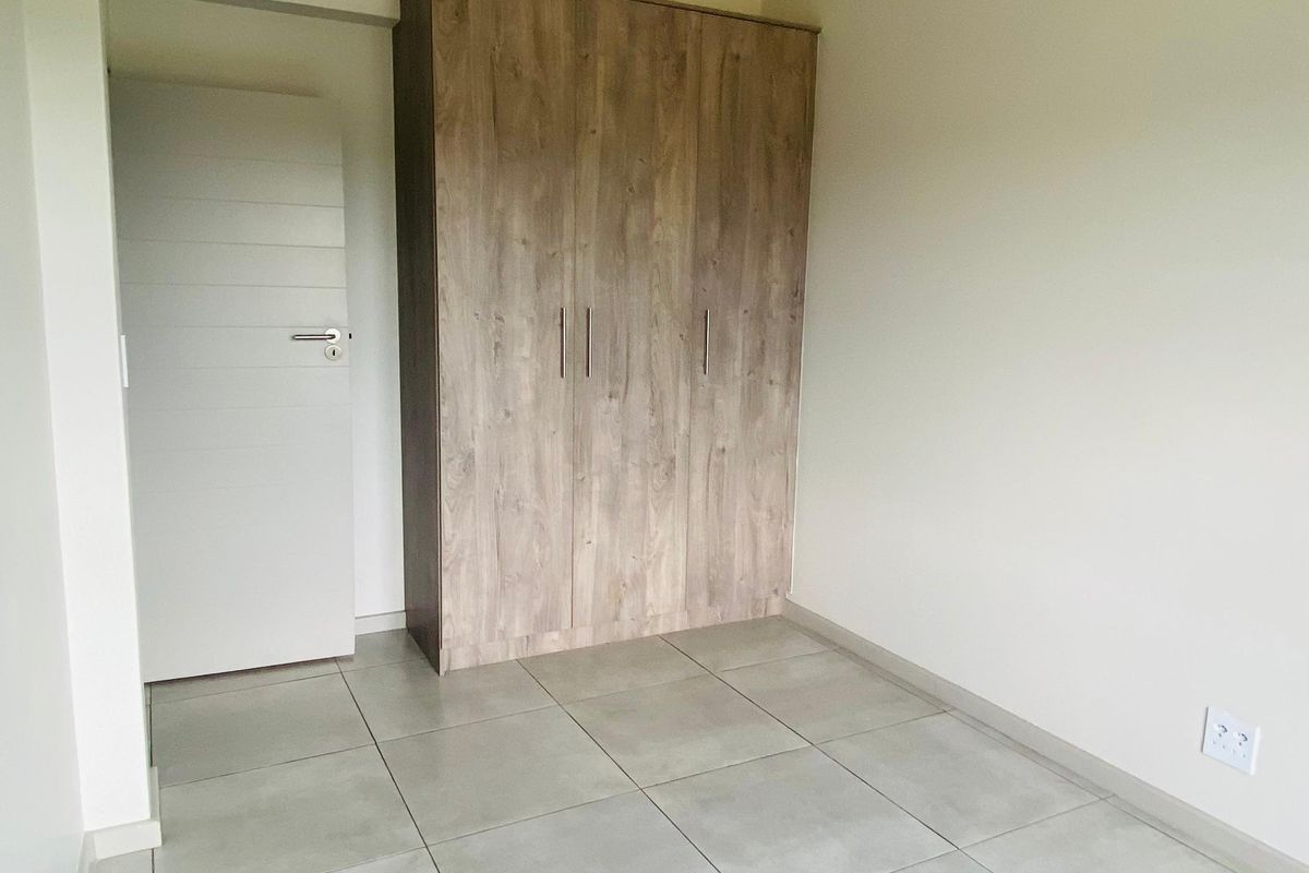 A clean, empty bedroom featuring neutral tiled flooring, a built-in wooden wardrobe, and a modern interior door.