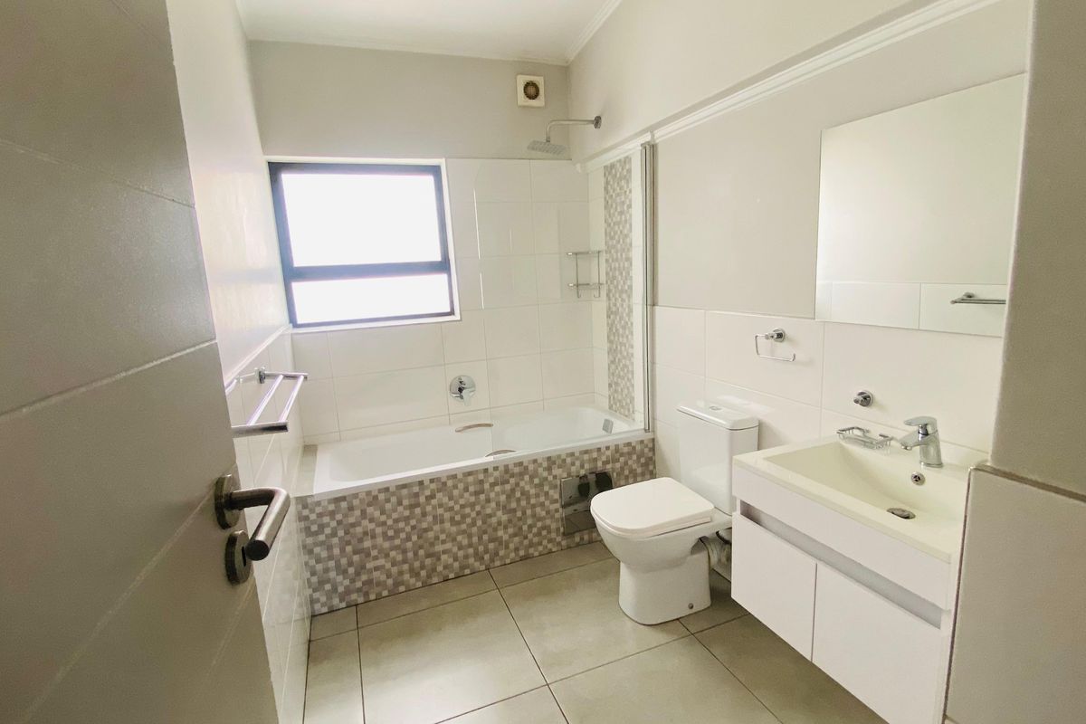A clean, modern bathroom featuring a built-in bathtub with shower head, wall-mounted vanity, toilet, and tiled finishes.