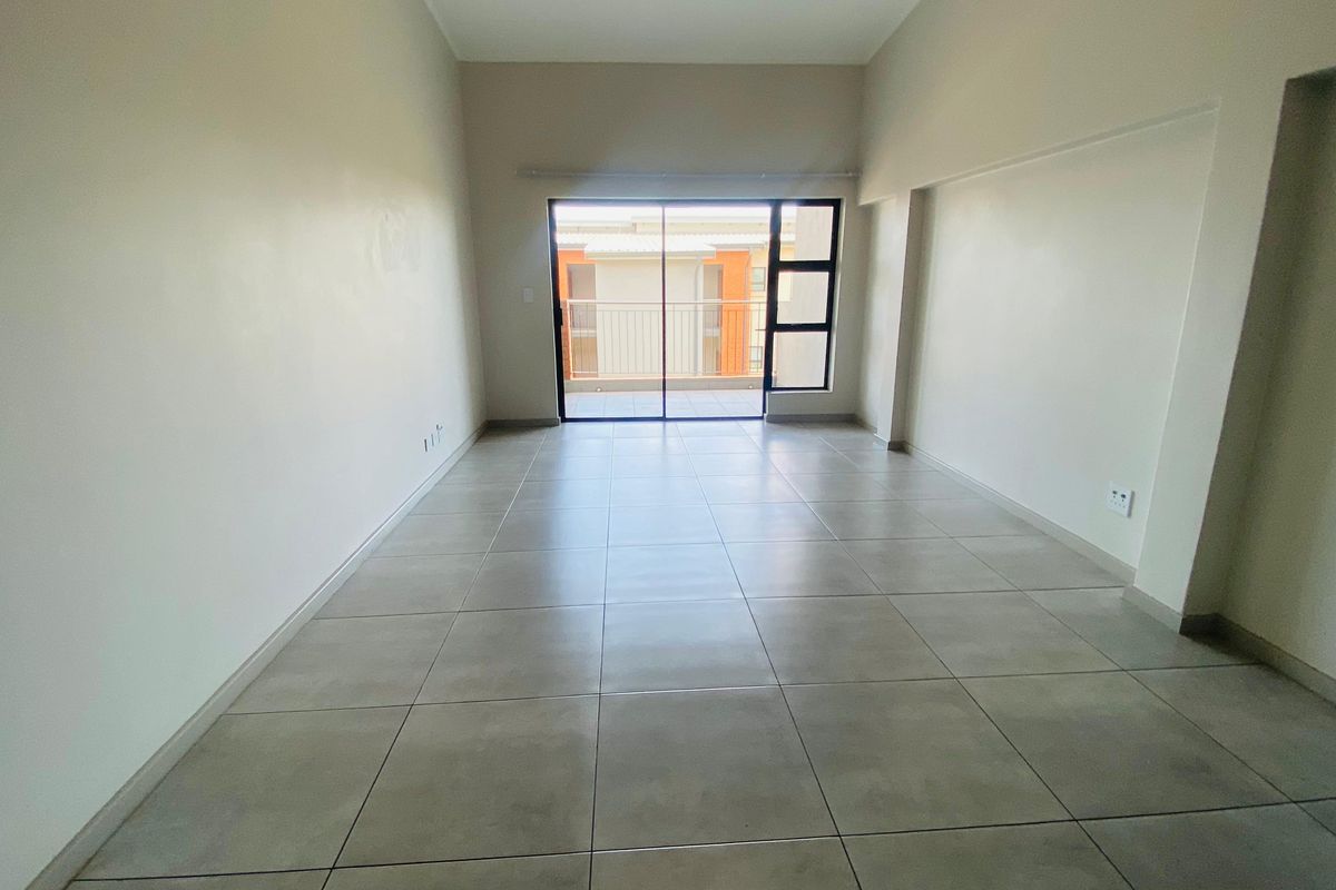 A spacious, empty living area featuring neutral tiled flooring and large sliding glass doors leading to an outdoor balcony.