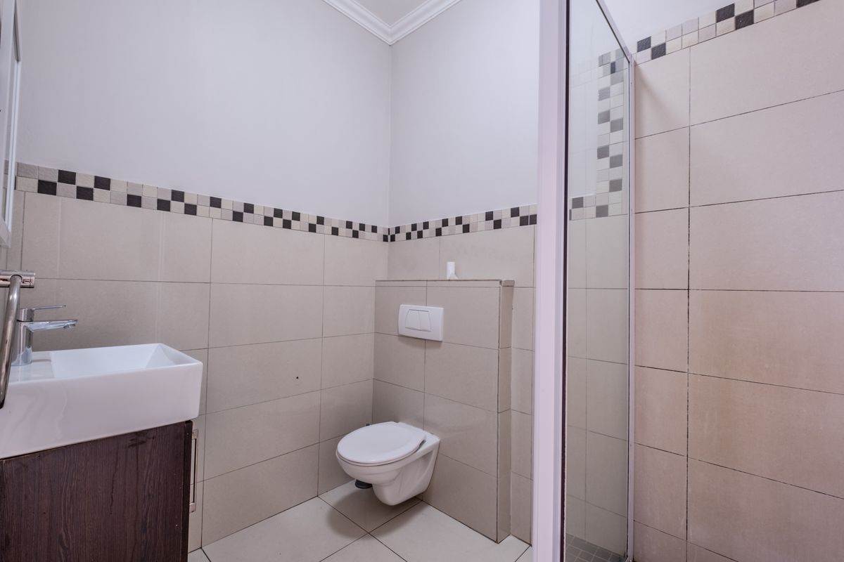 A clean, modern bathroom featuring a wall-mounted toilet, vanity basin, and a glass-enclosed shower with neutral tiled finishes.