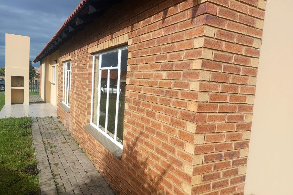 Rear exterior view of the house featuring face brick walls, a tiled roof, aluminium windows, and a built-in outdoor braai area.