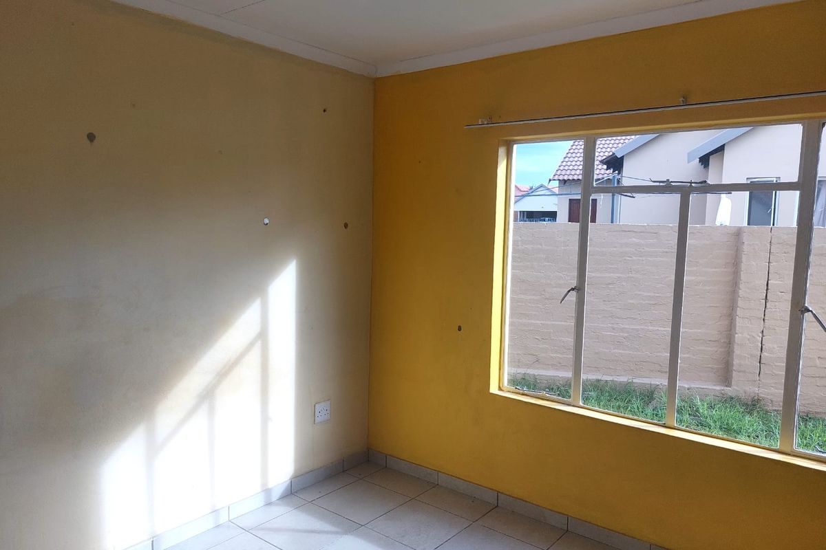 An empty bedroom featuring tiled flooring and a large window, requiring minor cosmetic updates to the wall surfaces.