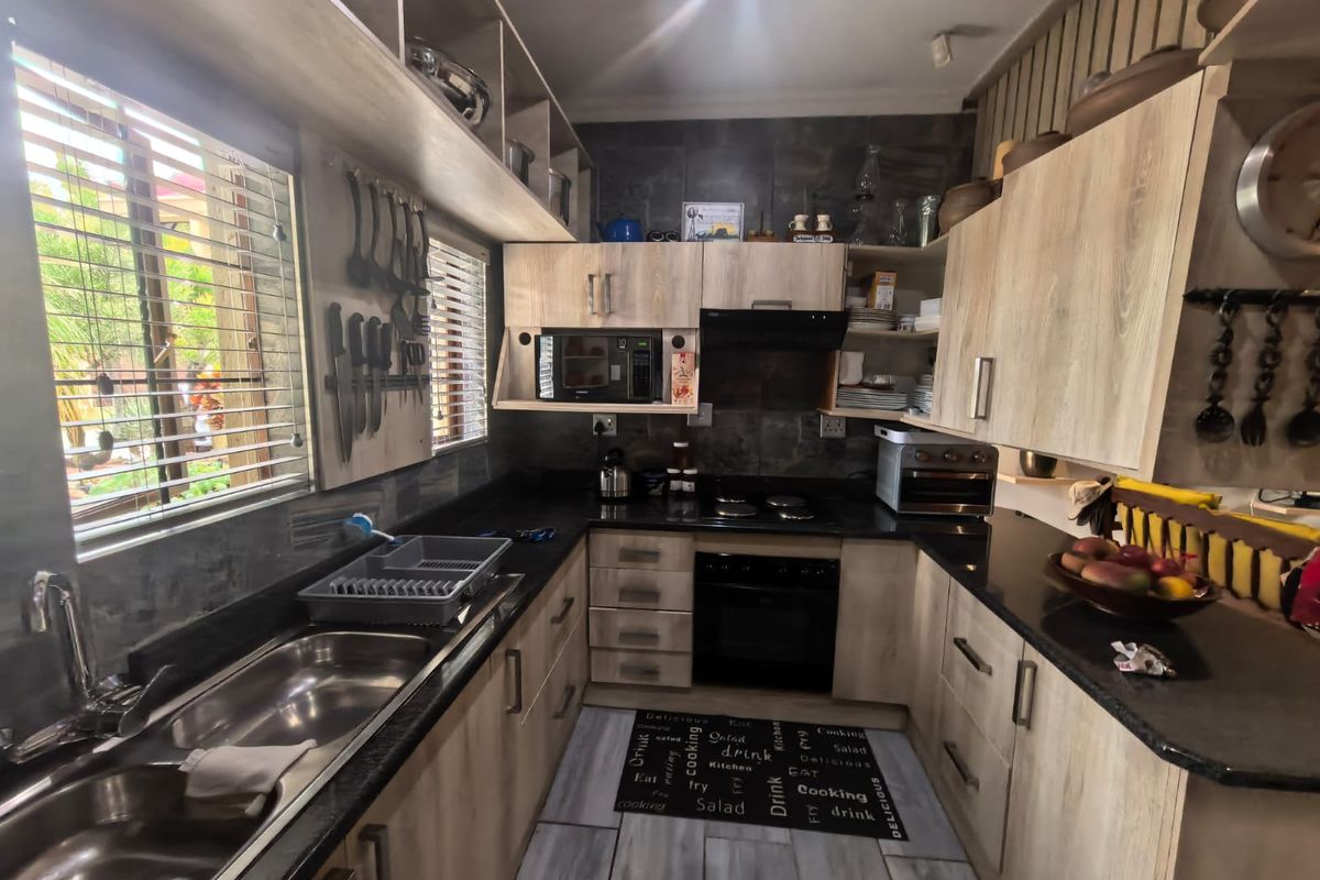 A functional kitchen featuring light wood-finish cabinetry, dark granite countertops, a double basin sink, and integrated appliances including an oven and hob.