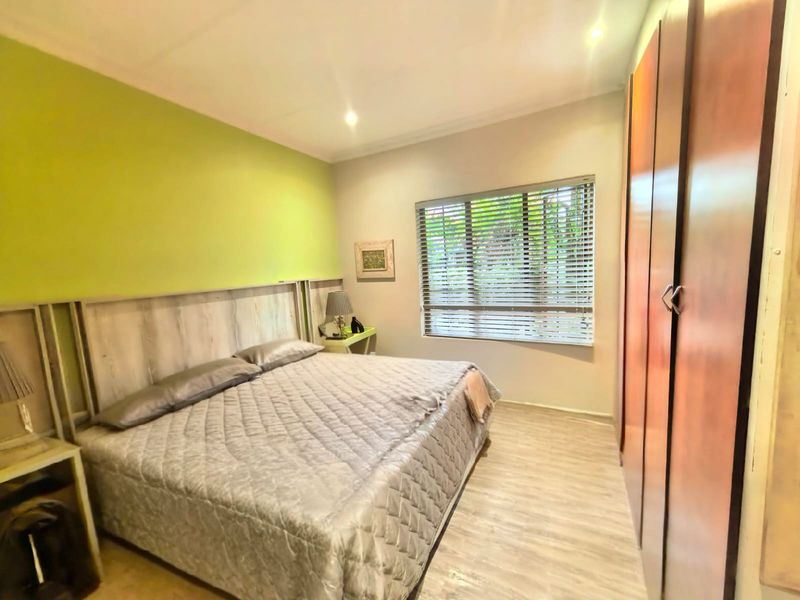 A bedroom featuring built-in wooden cupboards, laminate flooring, recessed lighting, and venetian blinds.