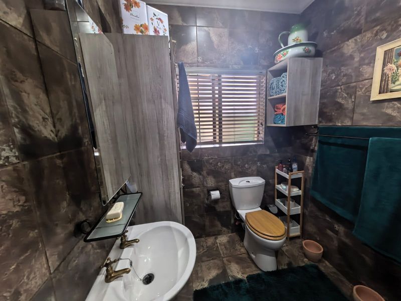 A compact bathroom featuring dark marble-effect wall and floor tiles, a pedestal basin, and a standard toilet with integrated shelving.