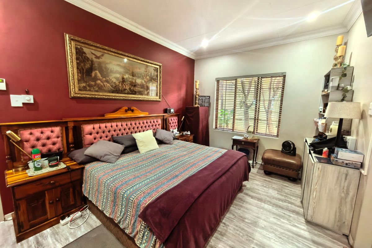 A bedroom featuring laminate flooring, recessed downlighting, and venetian blinds, with a bold accent wall and traditional crown molding.