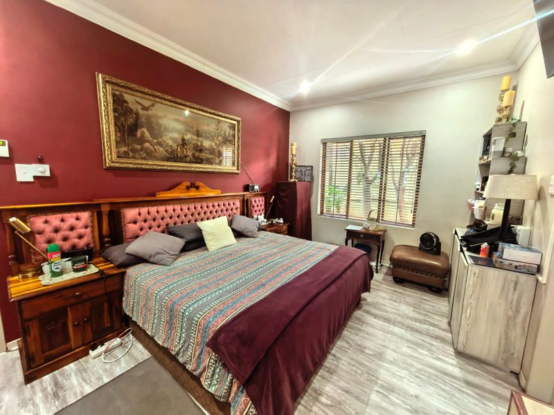 A bedroom featuring laminate flooring, recessed downlighting, and venetian blinds, with a bold accent wall and traditional crown molding.