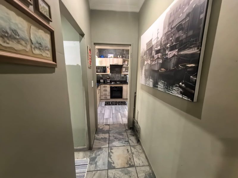 A view through a tiled hallway leading into a kitchen area with light wood cabinetry and dark countertops.