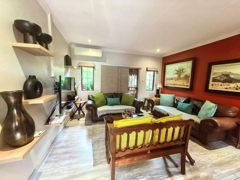A comfortable living room featuring laminate flooring, floating shelving, and a wall-mounted air conditioning unit, creating a functional and inviting space.