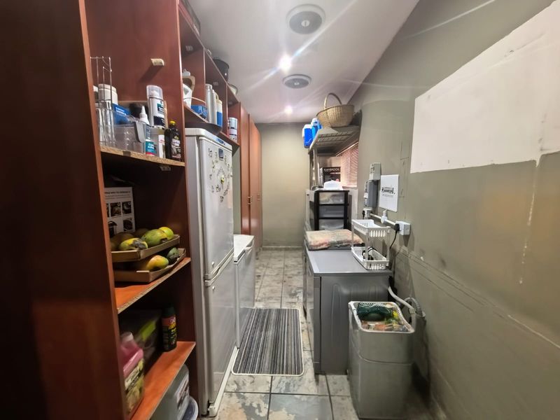 A functional scullery or utility area featuring built-in cabinetry, tiled flooring, and dedicated space for appliances, requiring some cosmetic updates to the walls and flooring.