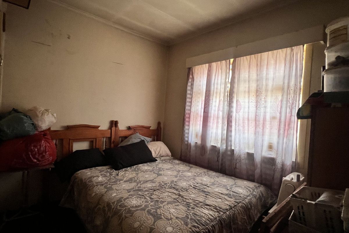 A bedroom featuring a window with curtains and visible wear on the wall surfaces, requiring cosmetic updates to improve the overall aesthetic.