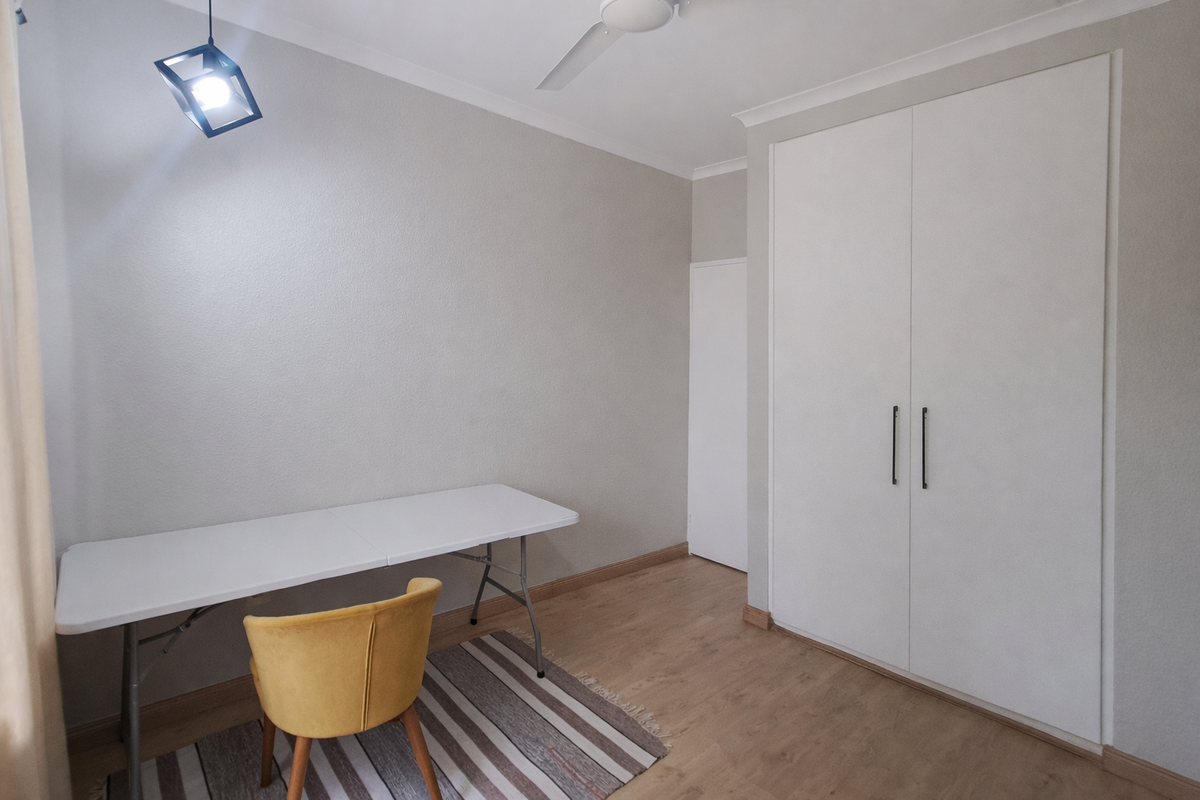A clean, neutral bedroom featuring laminate flooring, a built-in wardrobe, and a modern pendant light fixture.