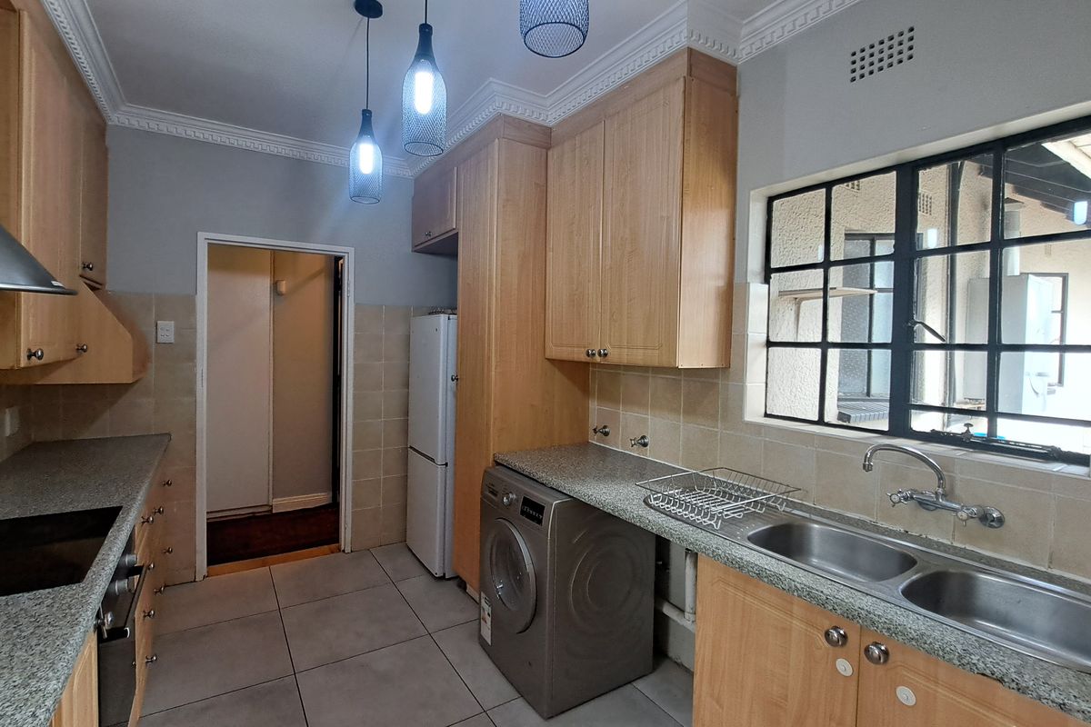 A functional kitchen featuring light wood cabinetry, granite countertops, a double basin sink, and tiled flooring with a classic coved ceiling finish.