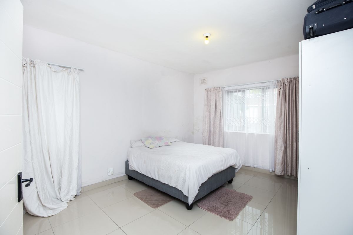 A bedroom featuring tiled flooring, a window with security bars, and built-in storage space.
