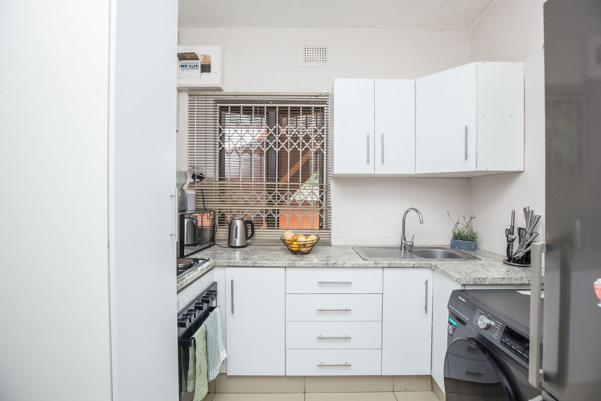 Compact kitchen featuring white cabinetry, stone-look laminate countertops, stainless steel sink, and built-in oven with hob.