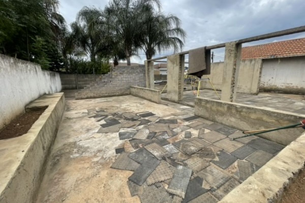 An unfinished rear outdoor area featuring concrete retaining walls, support pillars, and a paved patio space currently undergoing renovation or construction.