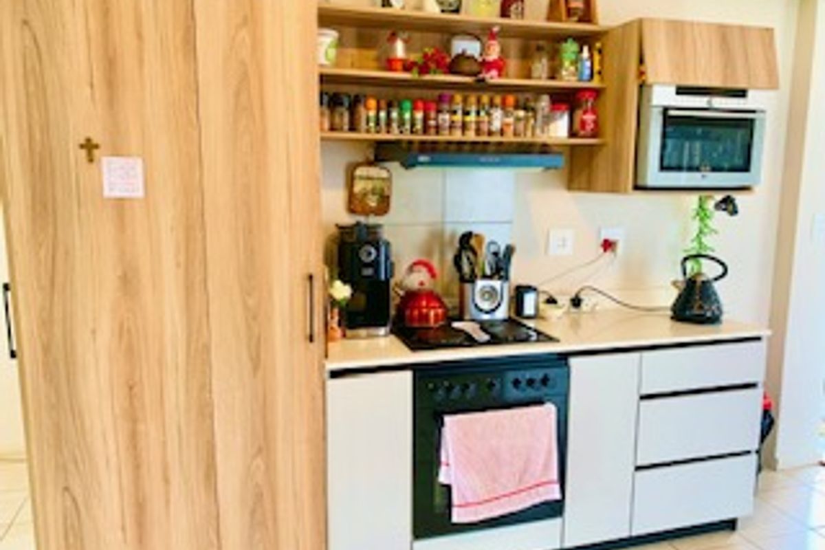 Compact kitchen featuring light wood-look cabinetry, built-in oven, electric hob, extractor fan, and integrated microwave with tiled flooring.