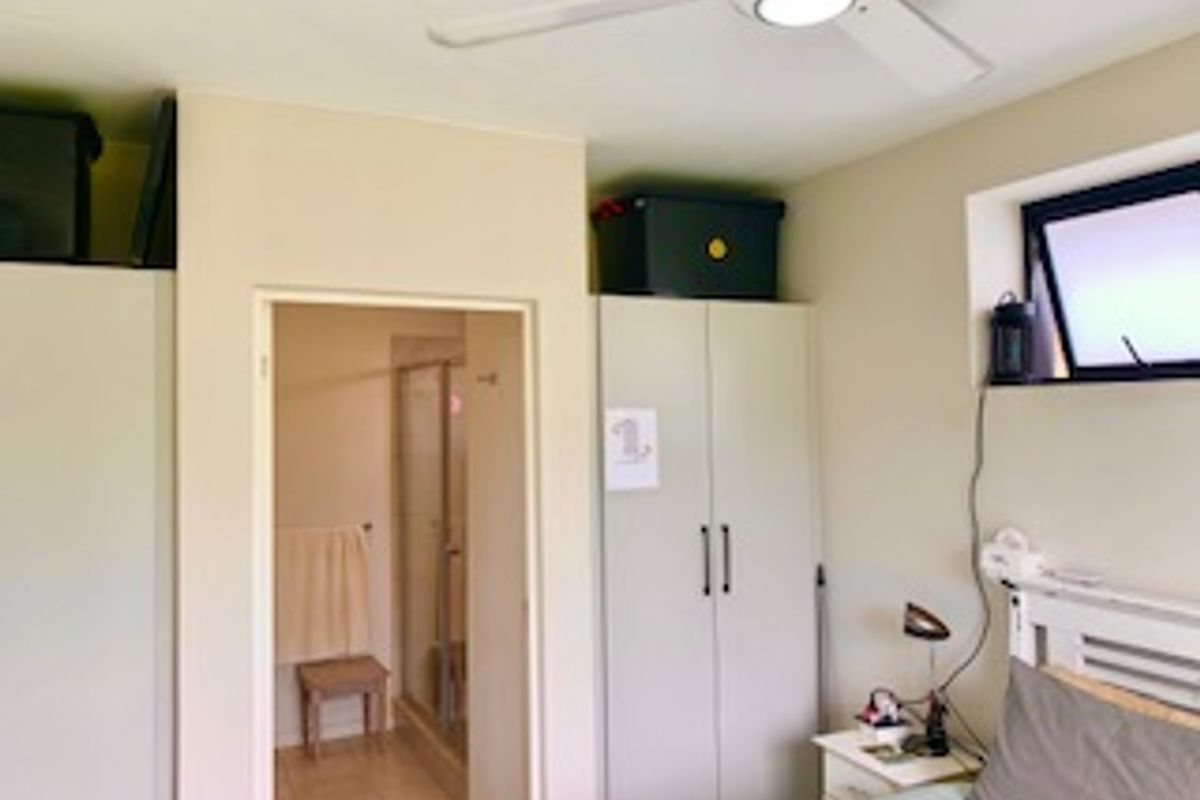 A bedroom featuring built-in cupboards, a ceiling fan, and an en-suite bathroom with a shower.