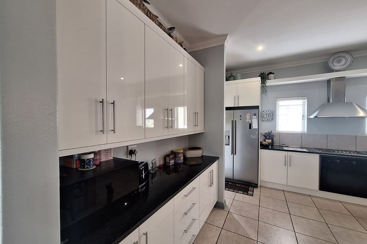 Modern kitchen featuring high-gloss white cabinetry, contrasting black granite countertops, stainless steel appliances, and durable tiled flooring.