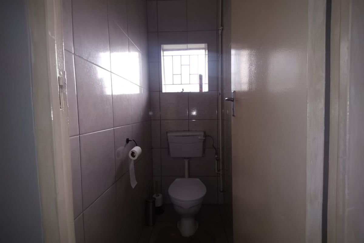 A compact guest bathroom featuring neutral wall tiles, a standard toilet, and a small window with security bars.