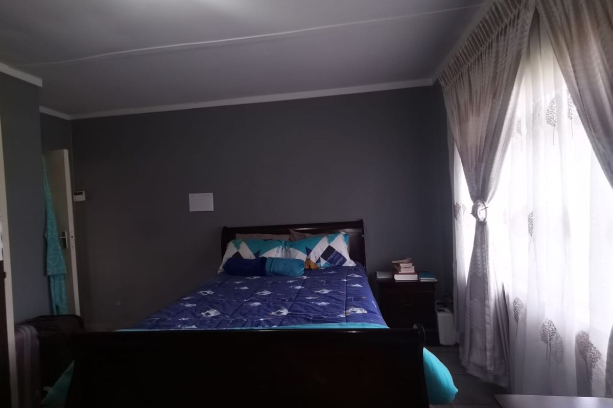 A bedroom featuring grey painted walls, tiled flooring, and decorative window curtains.