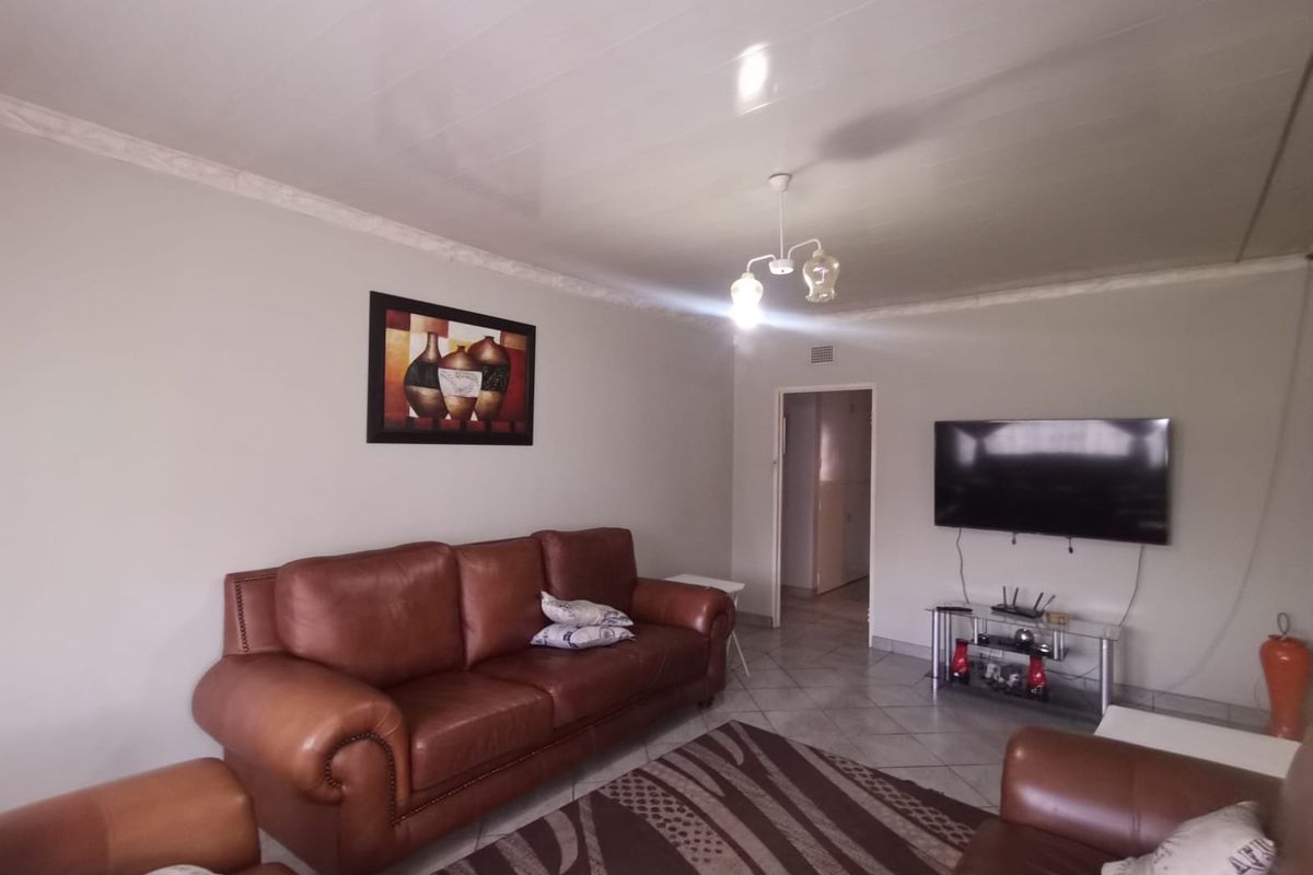 A living room featuring tiled flooring, decorative ceiling cornicing, and a glossy ceiling finish, providing a functional and neutral living space.