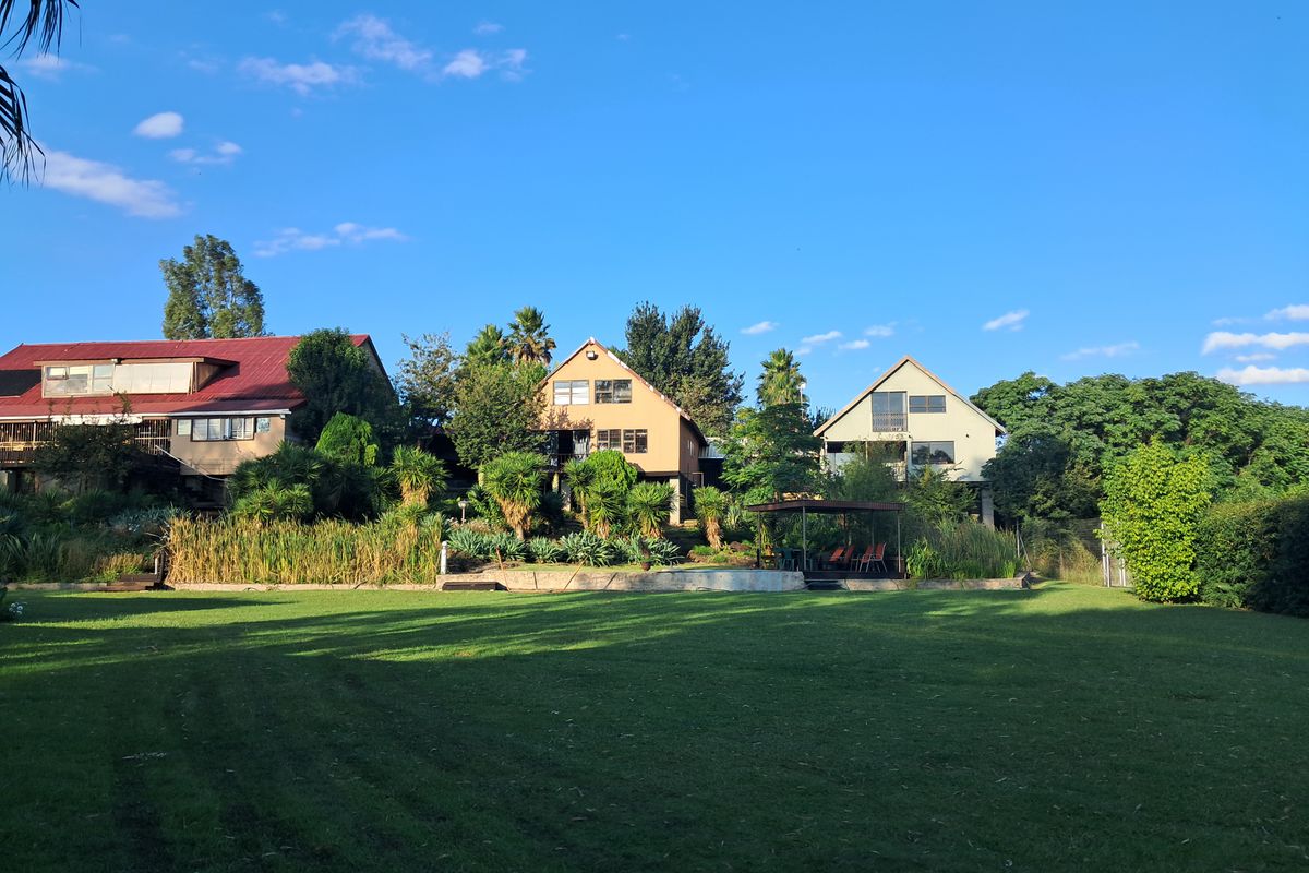 A wide-angle view of the rear garden area featuring expansive lawn, mature landscaping, and multiple residential structures in the background.
