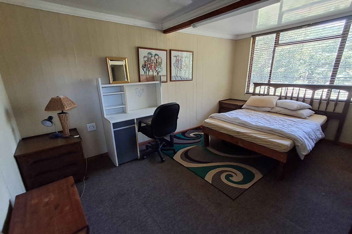 A bedroom featuring wood-paneled walls, large windows with horizontal blinds, and carpeted flooring.
