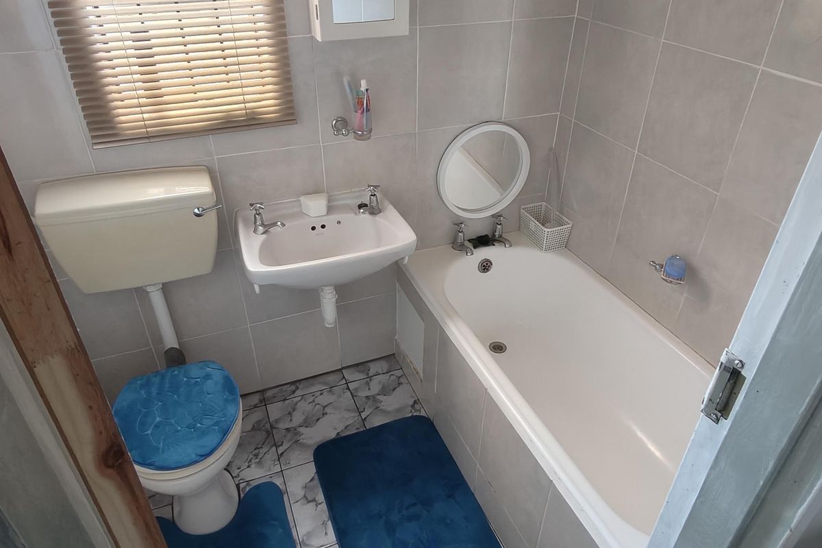 A functional bathroom featuring a bathtub, pedestal basin, and toilet with neutral wall tiling and a window for natural light.