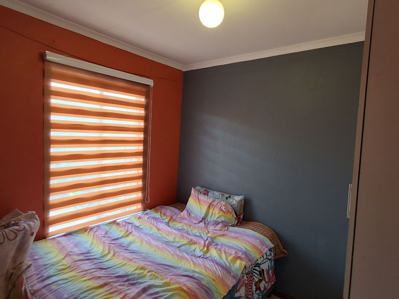 A bedroom featuring a built-in wardrobe, roller blind, and contrasting wall paint, providing a functional space for rest.