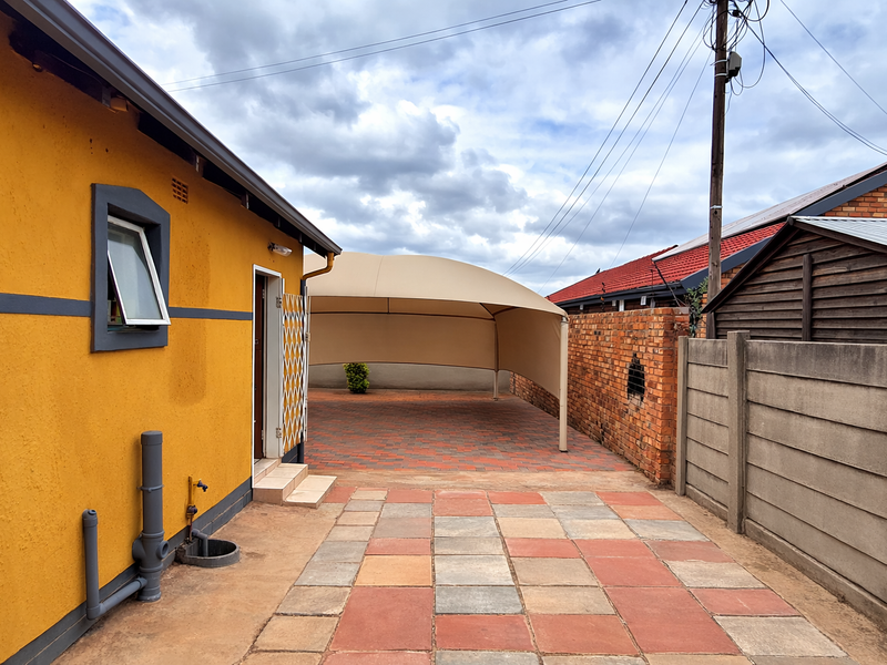 Rear exterior area featuring a paved driveway, a shade sail carport, and a combination of brick and precast concrete boundary walls.